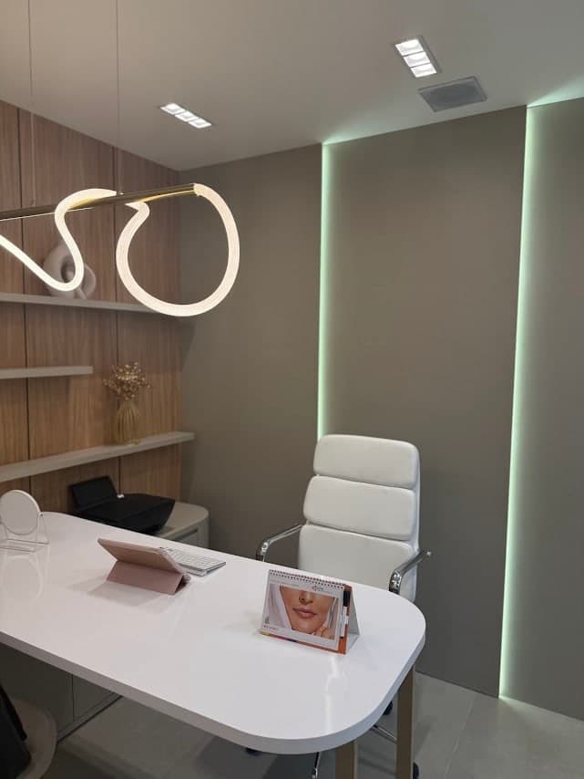 Sala de atendimento, com mesa branca e luminária de neon curvada